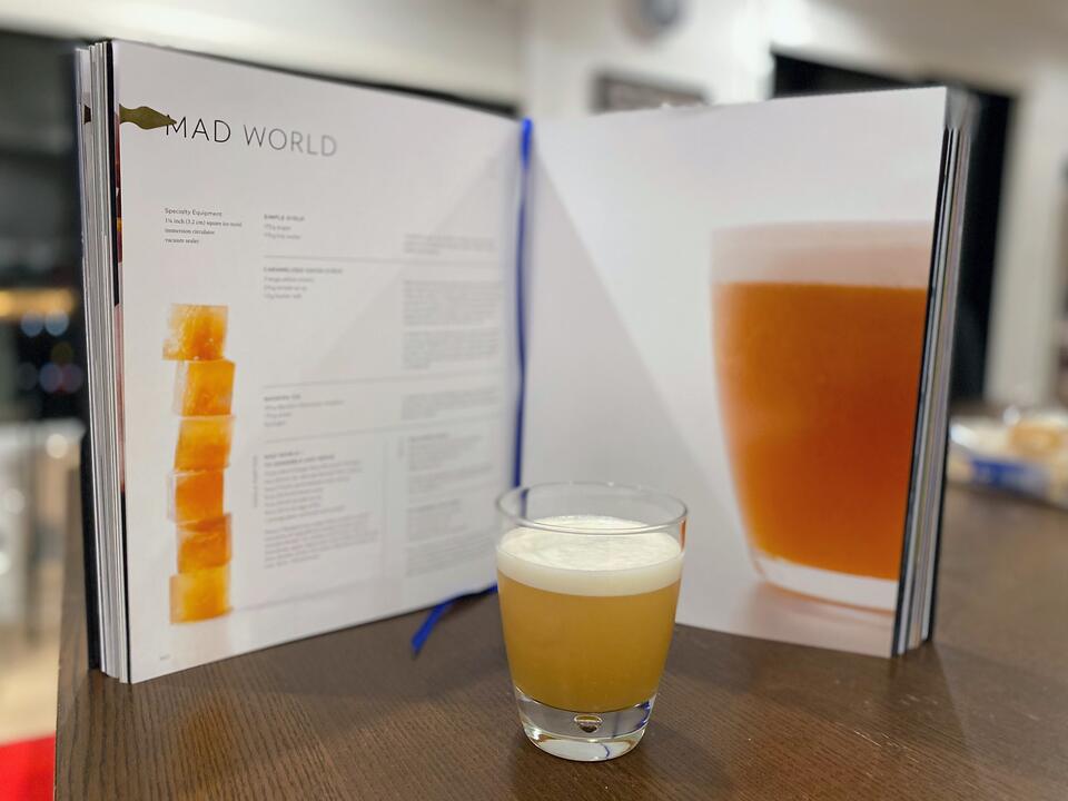 A photo of the Mad World in a double old fashioned glass, in front of the recipe from the Aviary Cocktail Book